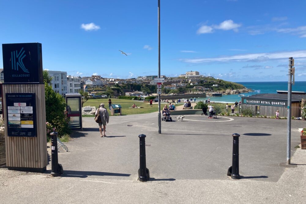 Killacourt entrance with bollards and signage as people make use of green space and seating