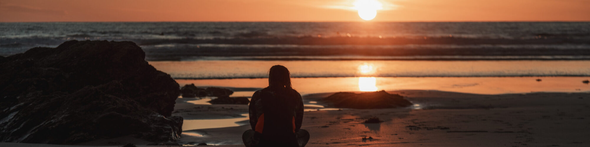 Contact Us at Newquay Town Council (Woman sitting on the beach at sunset)